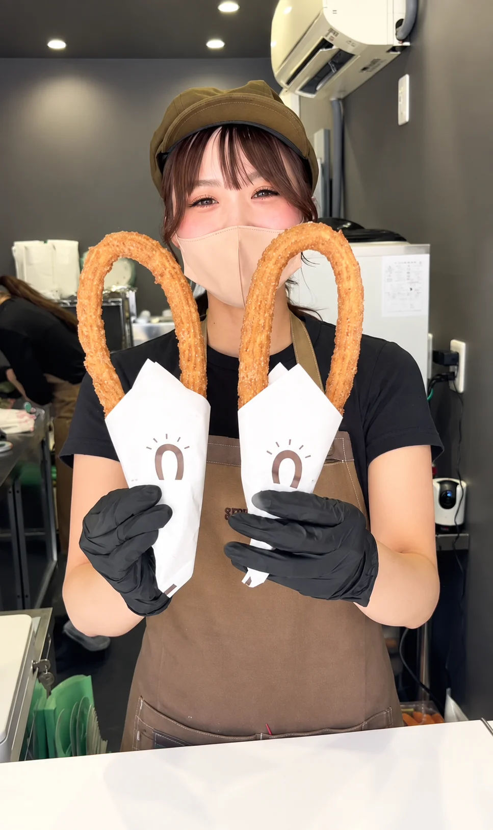 紙で包んだチュロスを2本持つ大須店のスタッフ